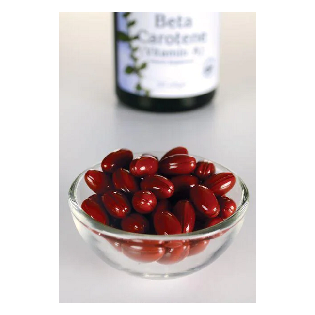 A glass bowl with red capsules is on a white surface. In the background, a blurred Swanson bottle labeled "Beta-Carotene (Vitamin A) 25000 IU 300 Softgels" suggests vision health promotion.