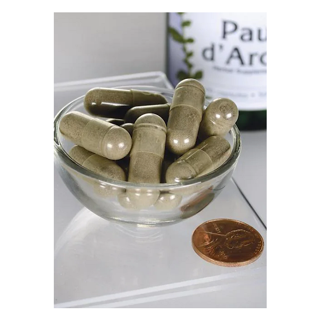 A Swanson Full Spectrum Pau d'Arco 500 mg bottle is partially visible behind a small glass bowl of greenish-brown capsules next to a penny, indicating the capsules' size and suggesting their antioxidant support for the immune system.