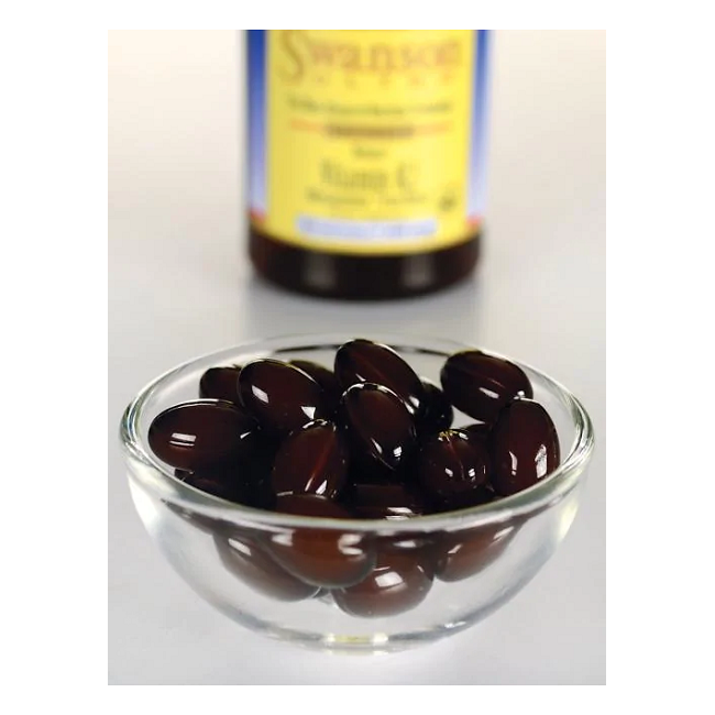 A glass bowl with dark brown capsules elegantly hints at the natural goodness of Menaquinone-7. In the background, a bottle of Swanson Vitamin K2-MK-7 100 mcg 30 Softgels evokes the traditional Natto source of Vitamin K2.