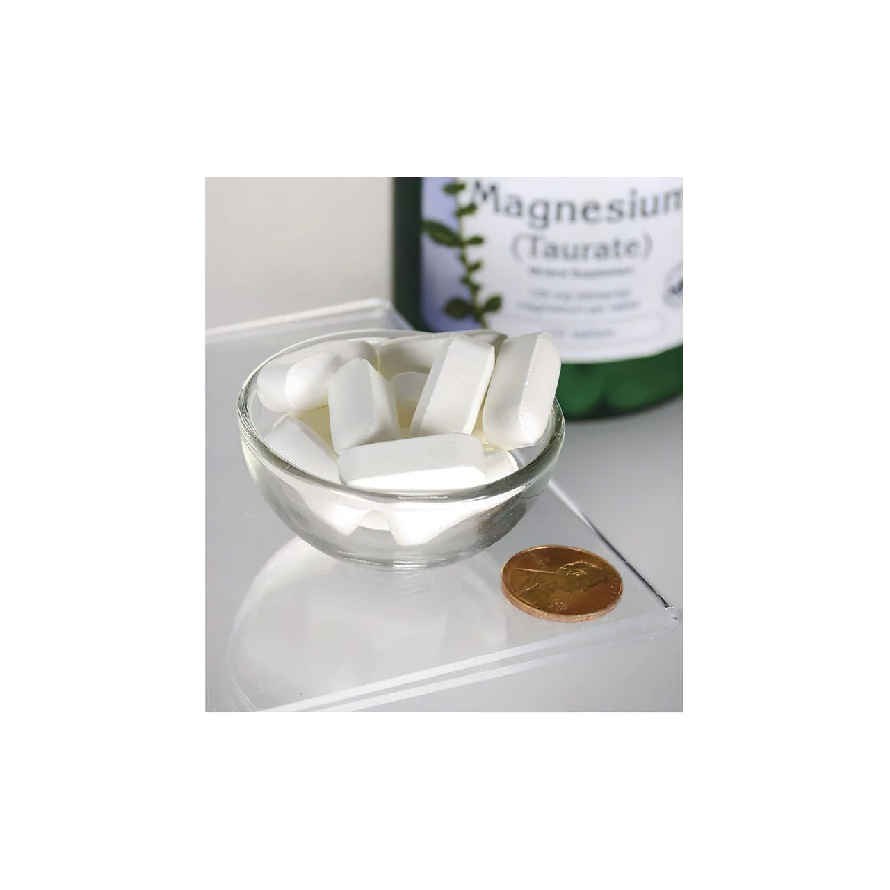 Un flacone di Swanson Magnesium Taurate 100 mg 120 tab seduto accanto a una ciotola di pillole bianche.
