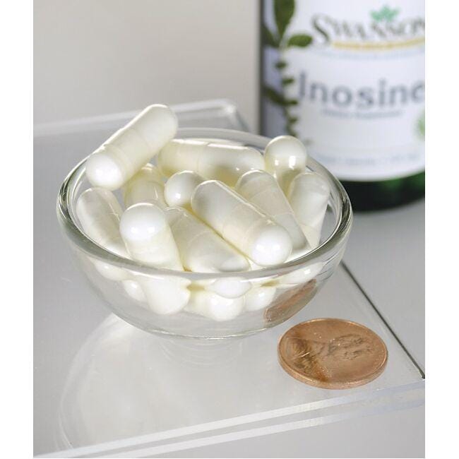 Una ciotola di pillole bianche accanto a un flacone di Swanson Inosine - 500 mg 60 capsule vegetali.