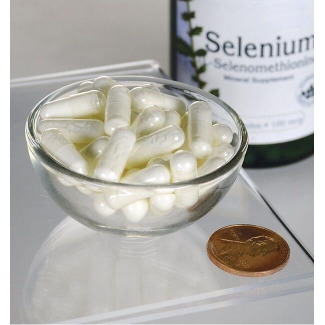 Swanson Selenio - 100 mcg 200 capsule L-Selenometionina in una ciotola accanto a un centesimo, offre un supporto antiossidante per la salute cardiovascolare.