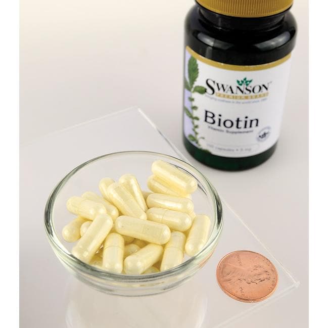 Un flacone di integratore alimentare Swanson Biotin - 5 mg 100 capsule accanto a un centesimo su un tavolo.