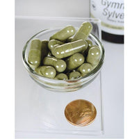 Miniatura di una ciotola di Swanson Gymnema Sylvestre Extract - 300 mg 120 capsule accanto a una moneta.
